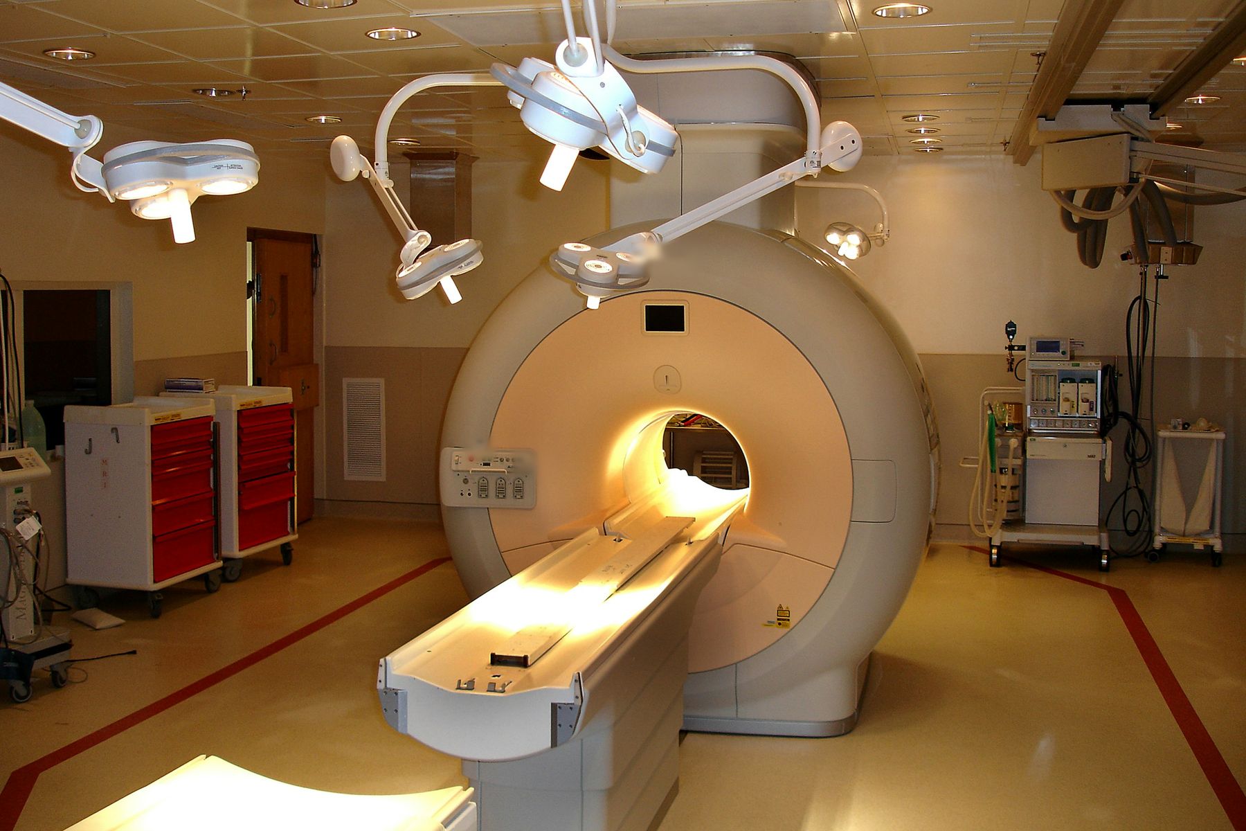 Salle d'IRM éclairée, l'anneau de l'appareil et sa table au centre, lampes au plafond