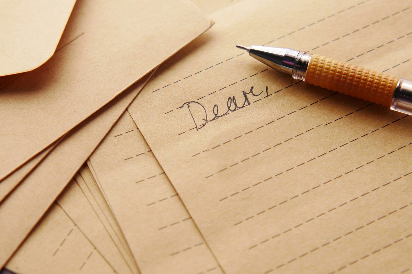 Enveloppes kraft et lettre manuscrite commencée, stylo posé dessus