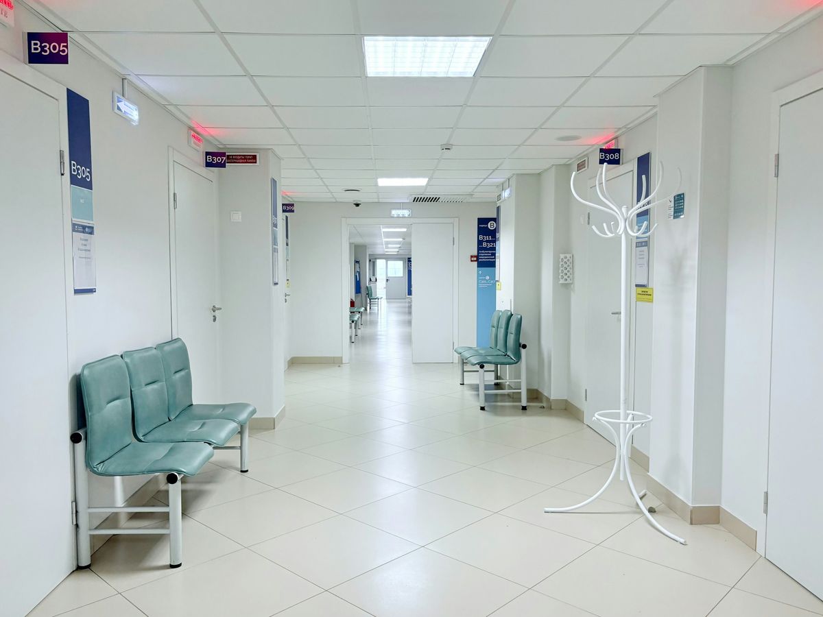 Couloir d'hôpital blanc et lumineux, chaises d'attente vertes et portes numérotées