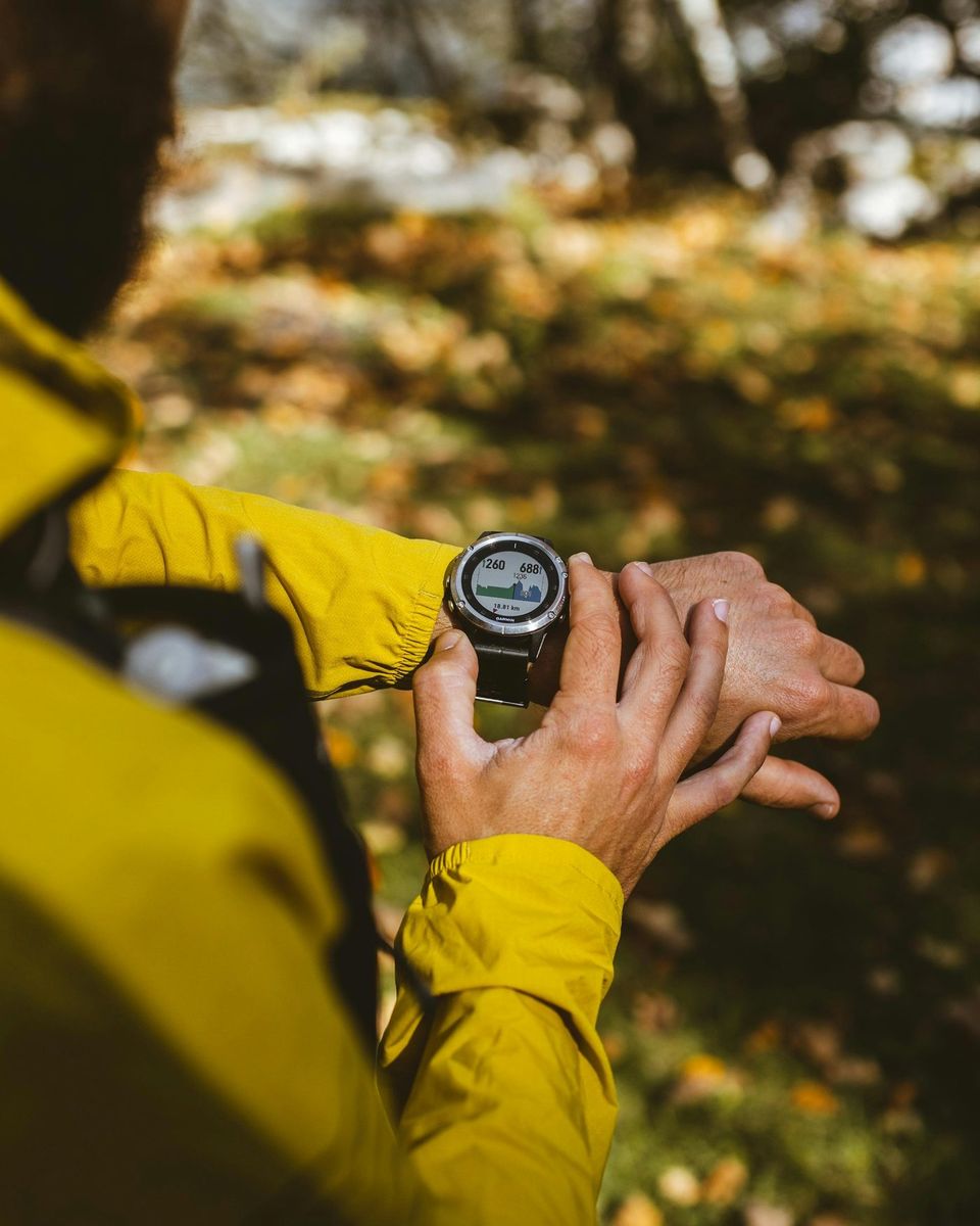 Personne en veste jaune consultant une montre ronde au poignet, en forêt