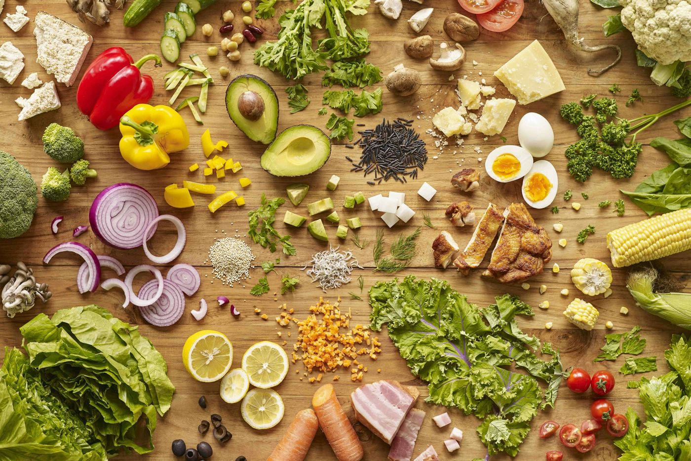 Table en bois couverte d'aliments variés : légumes, fruits, œufs, fromage, céréales et légumineuses
